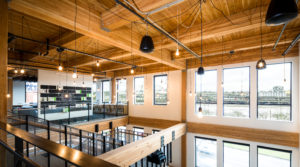 38 Davis, a mixed-use building in Portland, Oregon, features a timber frame structure with exposed glulam beams over a concrete podium. Additional exposed wood, brick and concrete elements throughout provide a distinct warehouse appeal in the open-layout office spaces, apartment units and community areas. Image Courtesy of Ankrom Moisan Architects