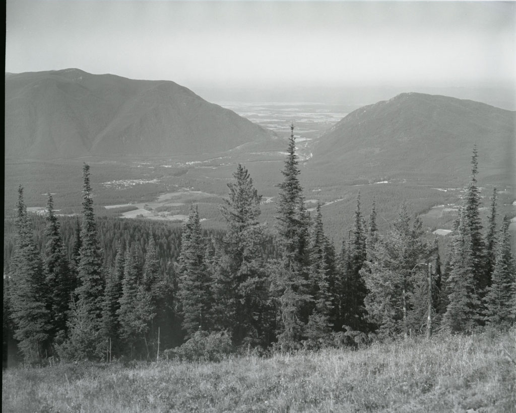 A photo of the same valley more than 40 years later mostly covered in lodgepole pine and Douglas fir. The photo is hazy because of smoke from a nearby wildfire. Date: 08/28/1981 Credit: George Gruell (USFS) Archived at the Mansfield Library at the University of Montana